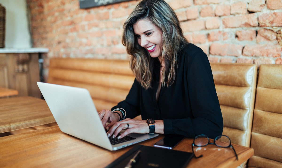 Smiling business woman writing on laptop at table