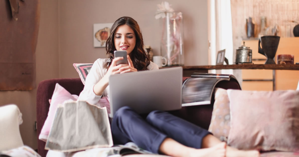 Image of a woman sitting on a sofa with a cell phone and laptop