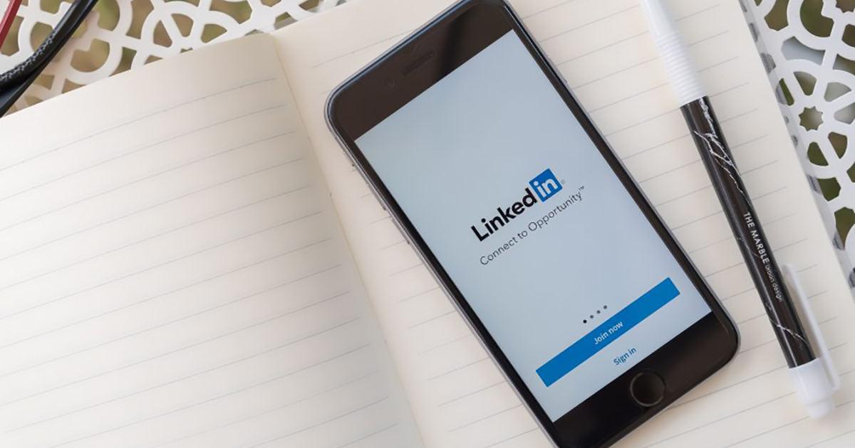 Smartphone displaying the LinkedIn login screen with the tagline “Connect to Opportunity,” placed on an open lined notebook beside a black-and-white pen.